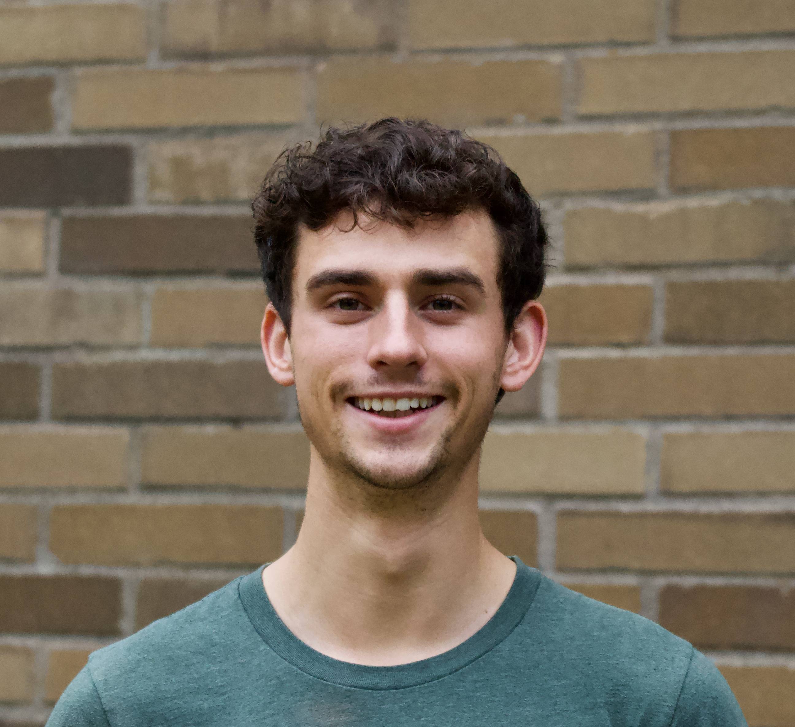 Joe Ewers, a white man with brown hair standing in front of a brick wall. 